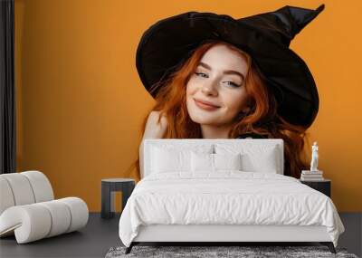 Smiling young woman in witch costume on orange background. Halloween celebration and party concept. Studio portrait of beautiful redhead girl. Carnival, masquerade. Banner with copy space Wall mural