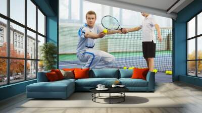 Instructor or coach teaching child how to play tennis on a court indoor Wall mural