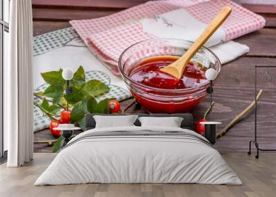 Closeup of rosehip jam in a glass bowl with hips and branches on a wooden table Wall mural