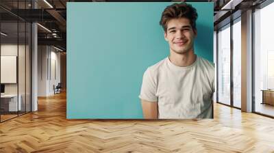 a smiling young man in casual attire standing confidently against a calming blue background Wall mural