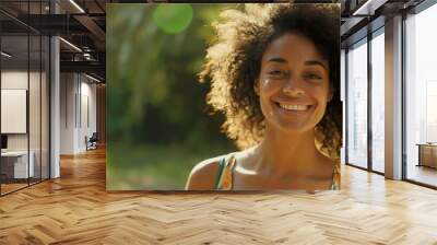 an ambitious woman with curly hair, smiling and standing casually in a summer outfit, against a fresh green backdrop, ideal for adding text or graphics. Wall mural