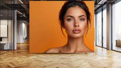 an image of a radiant woman with dark hair and healthy skin, posed against an orange background that exudes vibrancy and positive Wall mural