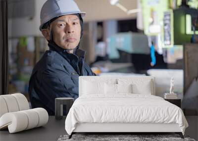 Supervisor of a manufacturing site wearing a white helmet with a machine tool in the background. Wall mural