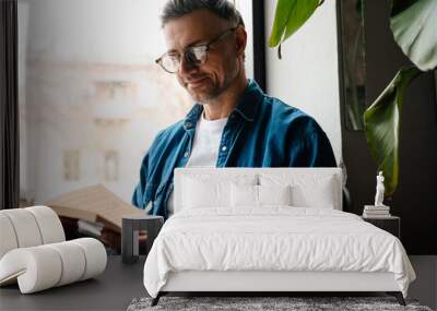 Adult handsome smiling man in glasses reading book Wall mural