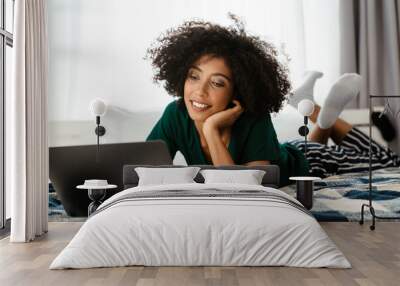 African american young woman lying in bed and using laptop at home Wall mural