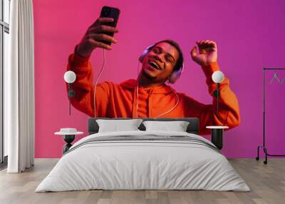 African man dancing while listening music with headphones and mobile phone isolated over pink neon background Wall mural