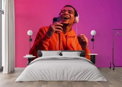 African man listening music with headphones and singing while holding smartphone like microphone isolated Wall mural