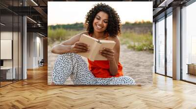 African woman reading a book at the beach outside Wall mural