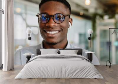 Afro american young man in eyeglasses and earphones standing indoors Wall mural