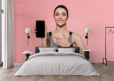 Amazing beautiful young pretty fitness woman showing display of mobile phone isolated over pink wall background. Wall mural