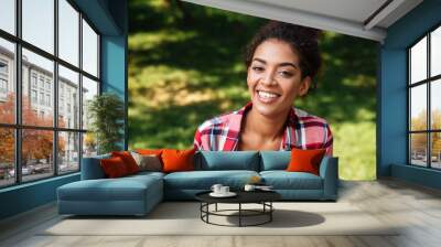 Amazing young african woman sitting outdoors in park Wall mural