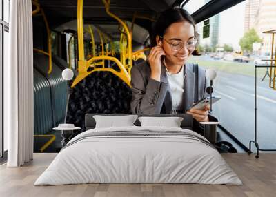 Asian woman in earphones looking at phone screen while traveling in bus Wall mural