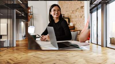 asian woman smiling while sitting at table with her colleagues during meeting in office Wall mural