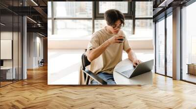 Asian young man studying with laptop while sitting by table at home Wall mural