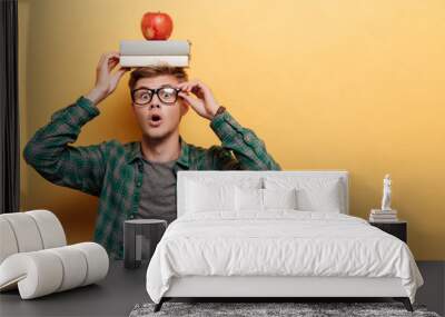 Astonished man student with book and apple on his head Wall mural