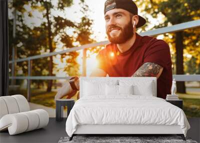 Attractive cheerful young man sitting at the skate park ramp Wall mural