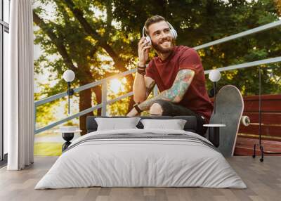 Attractive cheerful young man sitting at the skate park ramp Wall mural