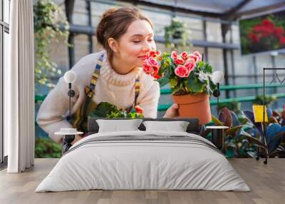 Attractive cute woman gardener smelling pink flowers in pot Wall mural