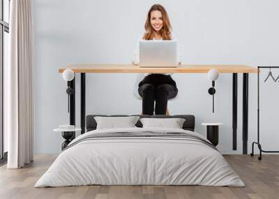 Attractive smiling businesswoman using laptop while sitting at office desk Wall mural