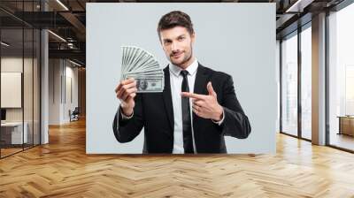 Attractive young businessman holding money and pointing on it Wall mural