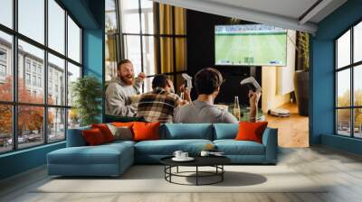 Back view of male friends playing football video game with gamepads at home Wall mural