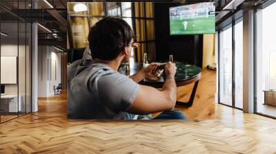 Back view of young white man playing football video game with gamepad Wall mural