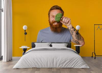 Bearded man holding broccoli while standing isolated over background Wall mural