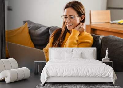 Beautiful caucasian pleased woman smiling and using laptop in apartment Wall mural