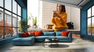 Beautiful caucasian woman smiling and using cellphone in apartment Wall mural