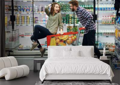 Beautiful couple having fun while choosing food in the supermarket Wall mural