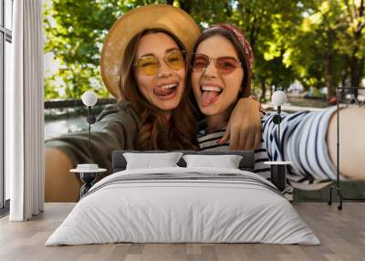 Beautiful excited women friends outdoors take a selfie by camera. Wall mural