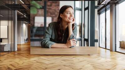 Beautiful happy woman smiling and looking aside while sitting at table Wall mural