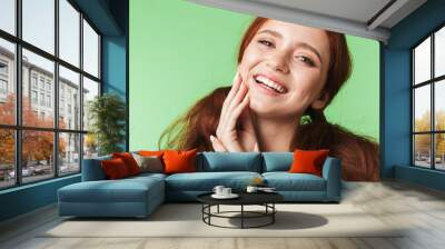 Beautiful happy young redhead girl posing isolated over green wall background. Wall mural