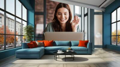 Beautiful smiling woman waving hand and working with laptop Wall mural