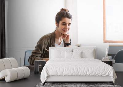 Beautiful young concentrated woman using laptop computer indoors writing notes in notebook. Wall mural