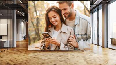 Beautiful young couple in love using mobile phone Wall mural