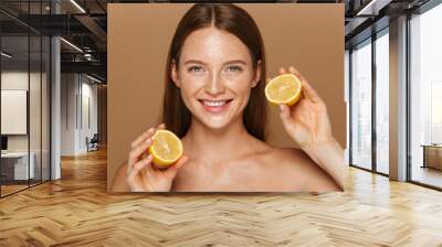 Beauty image of pretty shirtless woman with long hair holding two pieces of orange, isolated over beige background Wall mural