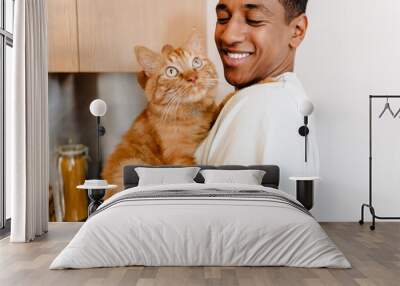 Black man wearing t-shirt smiling while petting his cat Wall mural