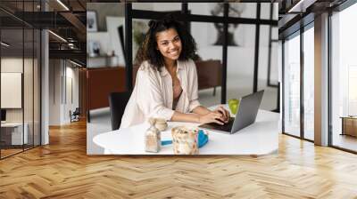 Black young woman smiling and working with laptop at home Wall mural