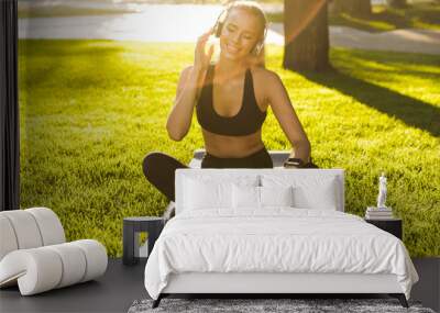 Blonde sports woman in park outdoors listening music with headphones. Wall mural