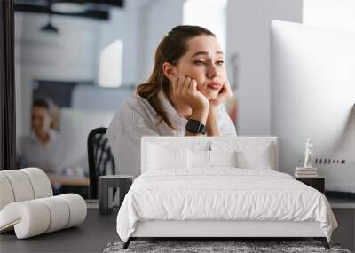 Bored young woman dressed in shirt sitting at her workplace Wall mural