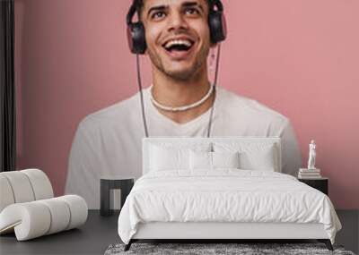 Brunette young man in headphones smiling while using mobile phone Wall mural