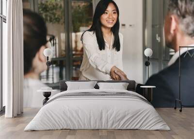 Business, career and placement concept - image from back of two employers sitting in office and shaking hand of young asian woman, after successful negotiations or interview Wall mural