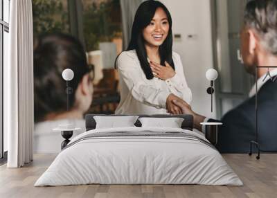 Business, career and placement concept - two business partners in office shaking hand of young asian woman, after successful negotiations or interview Wall mural