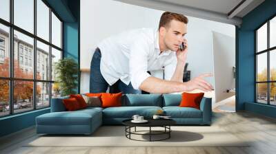 Businessman talking on mobile phone and using computer in office Wall mural