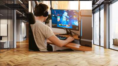 Caucasian brunette guy in headphones playing video game on his computer Wall mural