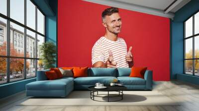 Caucasian man 30s in striped t-shirt gesturing index finger on camera meaning hey you, isolated over red background Wall mural