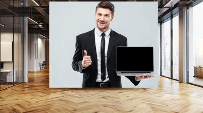 cheerful businessman holding blank screen laptop and showing thumbs up Wall mural