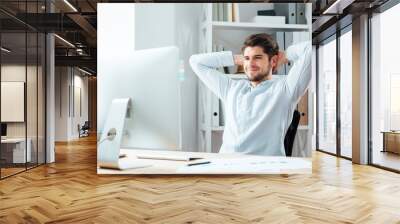 Cheerful businessman sitting at the table with laptop and stretching Wall mural