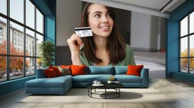 Cheerful nice woman using credit card while working with laptop Wall mural